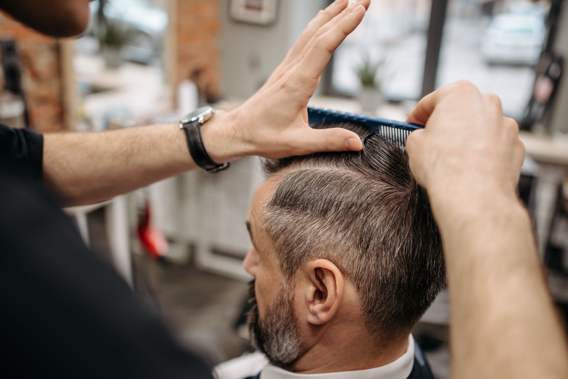 Close-up of a barber styling a customer's hair in a modern barbershop setting.